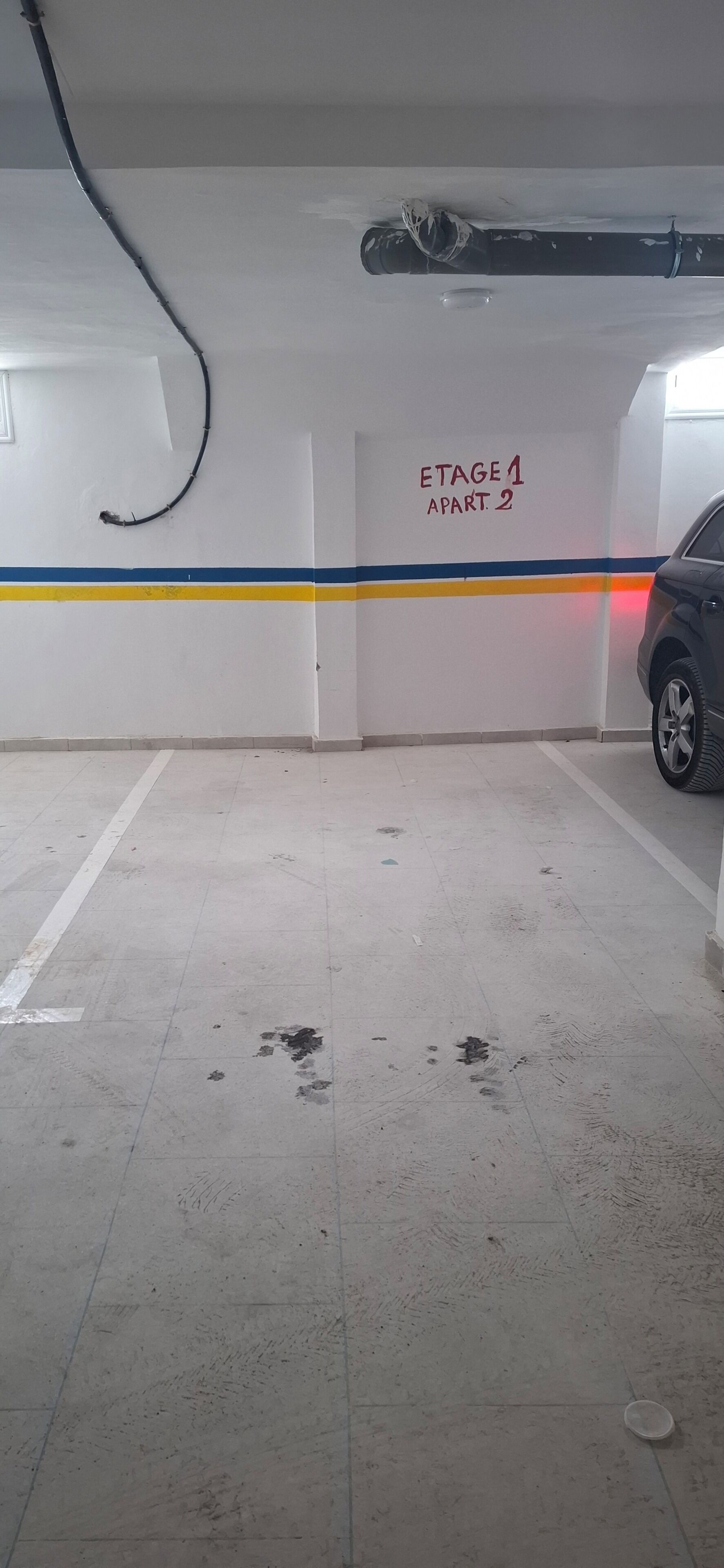 Eine überdachte Parkgarage mit weißem Boden, einem blauen und gelben Streifen und einem Schild mit der Aufschrift 'Stage 1 Apartment 2'.
