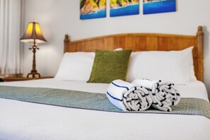 A neatly made bed with a rolled towel, a green pillow, and a lamp on a bedside table. - Maui Kamaole #K-104 Quiet Location, Close to Resort Pool, A/C (Kihei)
