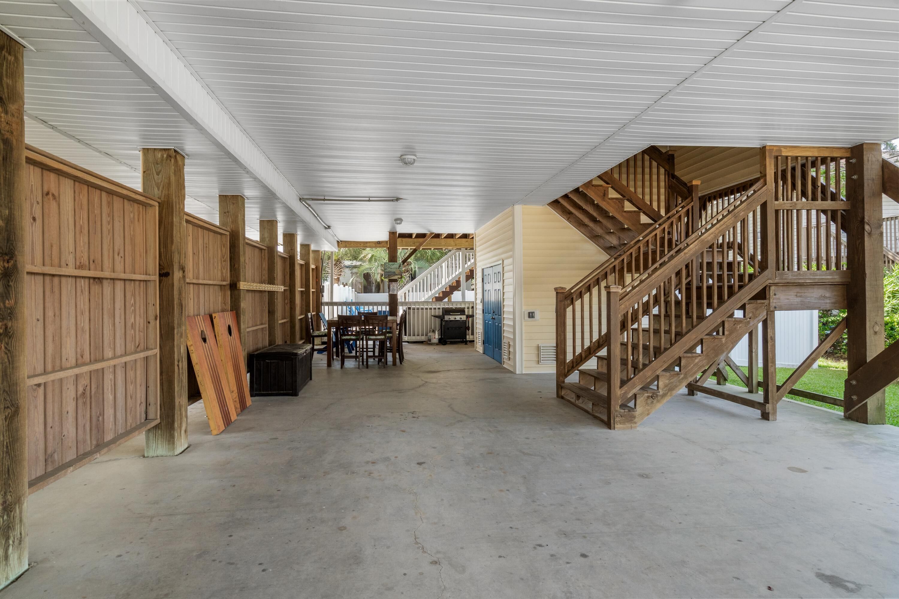 A covered outdoor area with a wooden staircase leading to a deck, a dining table with chairs, and a grill.