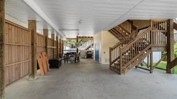 A covered outdoor area with a wooden staircase leading to a deck, a dining table with chairs, and a grill.