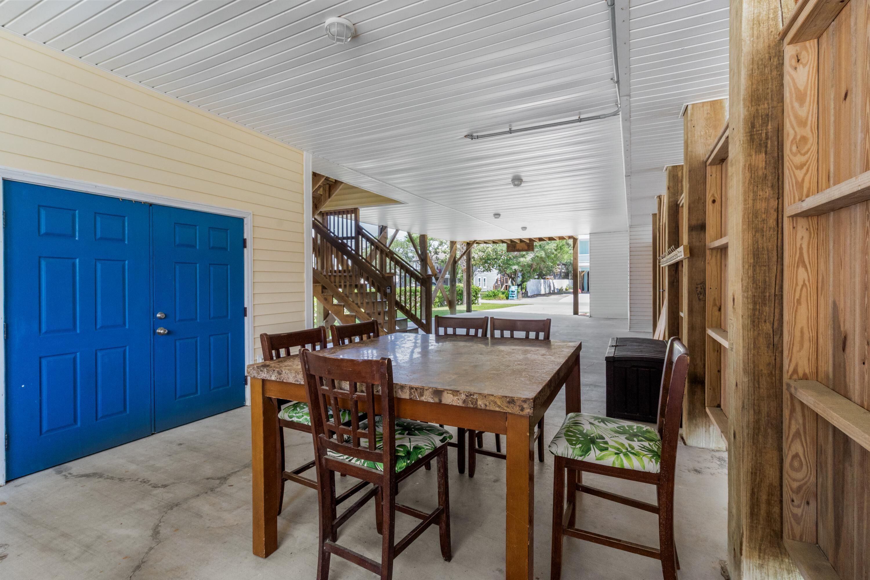A covered outdoor area with a dining table and chairs, a blue door, and a staircase leading to a covered porch.