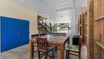 A covered outdoor area with a dining table and chairs, a blue door, and a staircase leading to a covered porch.