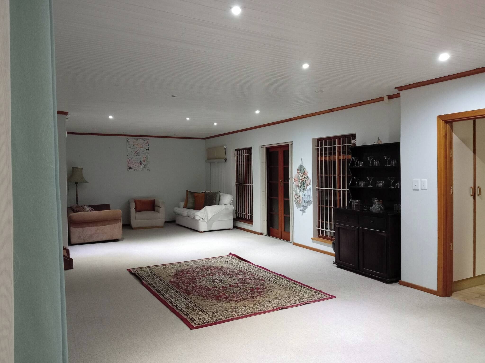 A spacious living room with a large rug, a sofa set, a cabinet, and a door leading to another room.
