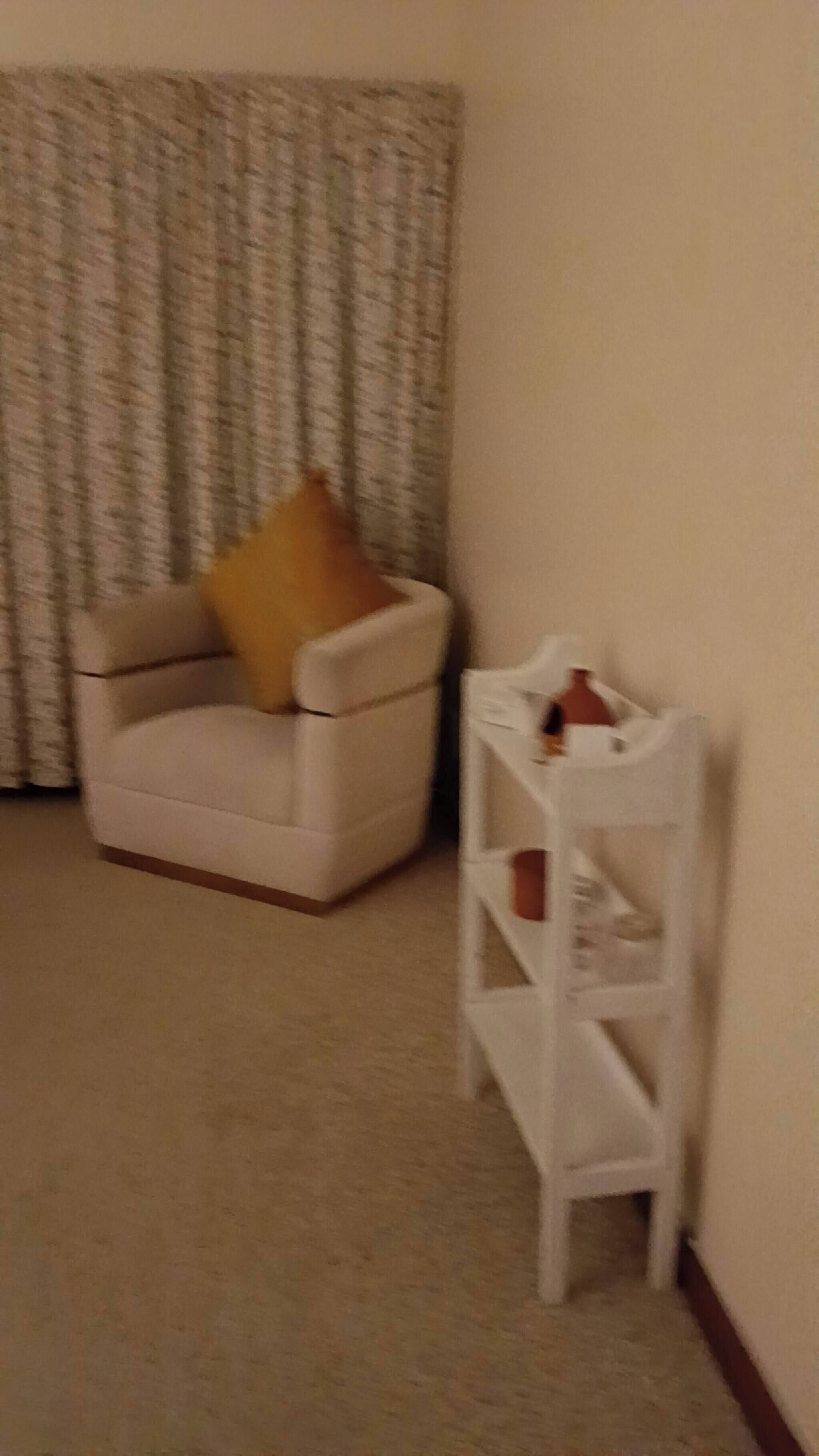 A room with a white armchair, a white side table, and a patterned curtain.