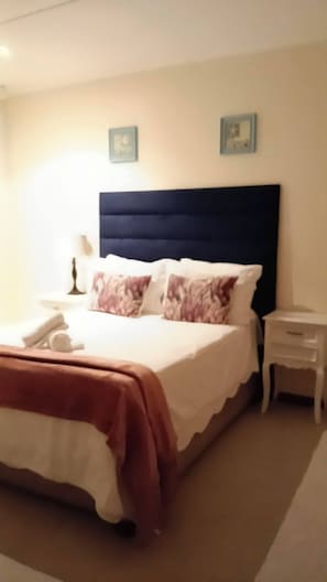 A hotel room with a bed, a bedside table, a nightstand, and two wall-mounted picture frames. - The Victorian Villa House (Great Kei)