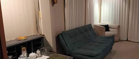 A room with a sofa, a table with kitchenware, and curtains.