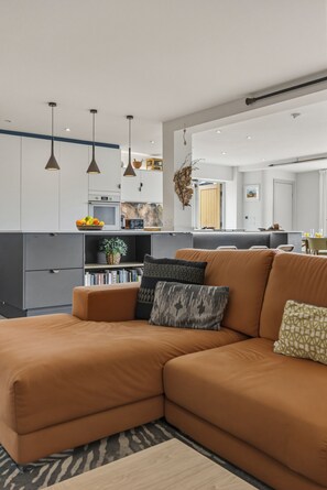 Ein modernes Wohnzimmer mit einer Eckcouch, einem Bücherregal und einem Essbereich mit Tisch und Stühlen.