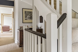 Eine Treppe mit weißen Geländern und einem hölzernen Handlauf, die zu einer Zwischenebene mit einem gerahmten Bild und einem kleinen Tisch mit Dekorationen führt.