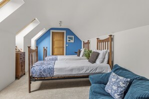 Ein Schlafzimmer mit geneigter Decke, einem hölzernen Bett, einer blauen Wand und einer Holzkommode.