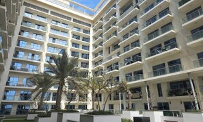 A multi-story residential building with balconies, large windows, and palm trees. - Sea View | Duplex Unit | Al Marjan Island | RAK (Ras Al Khaimah)