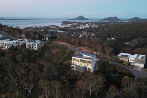A residential area with modern houses, a road, and a view of the sea and distant mountains.
