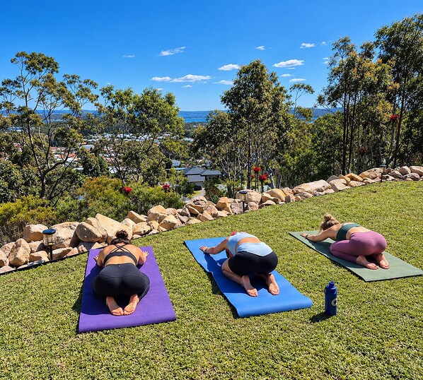 Three individuals practicing yoga on mats in an outdoor setting with a view of a residential area and hills in the distance.