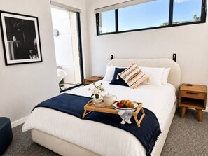 A modern bedroom with a bed, bedside tables, a tray with breakfast, and a window.