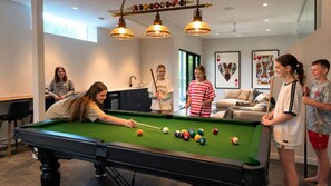 A pool table in a room with a modern design, including pendant lighting and framed artwork on the walls.