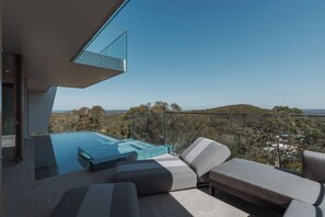 A modern outdoor lounge area with a glass-enclosed infinity pool, a comfortable seating arrangement, and a scenic view of the surrounding landscape.