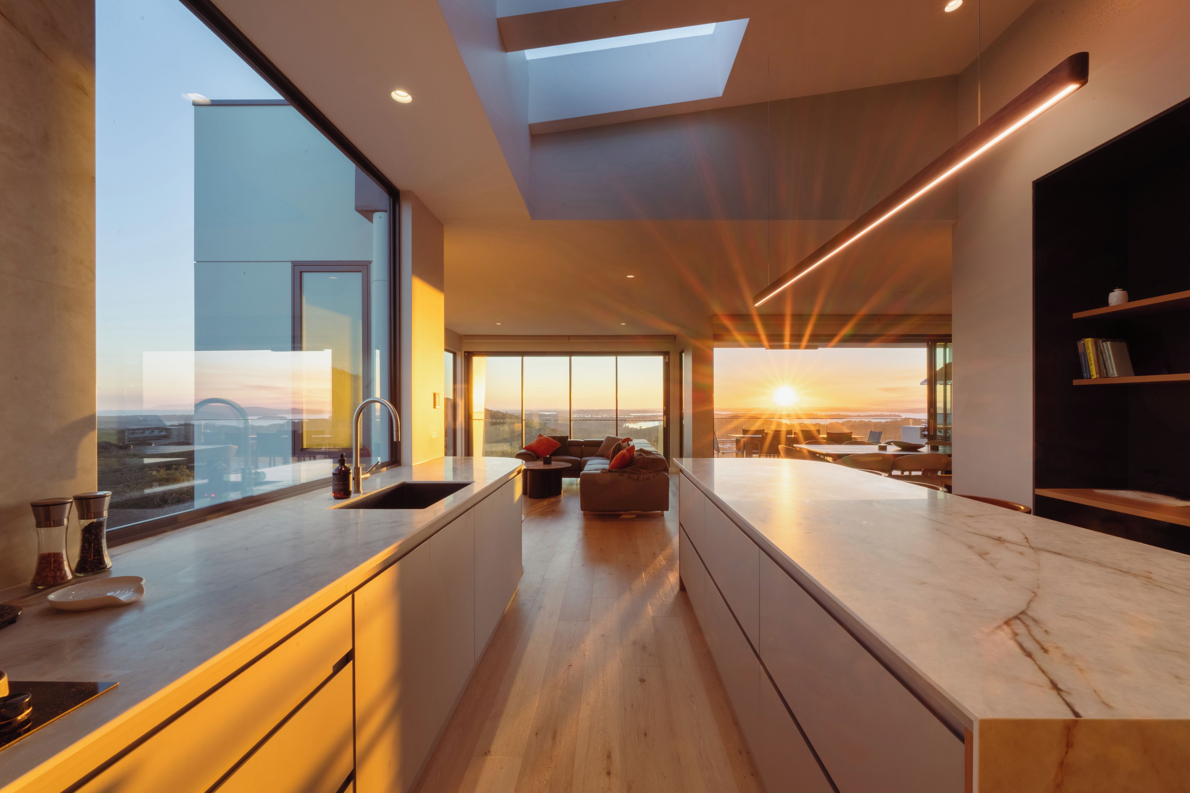 Une cuisine moderne dotée d’un grand îlot central, d’un coin repas et offrant une vue sur le coucher de soleil.
