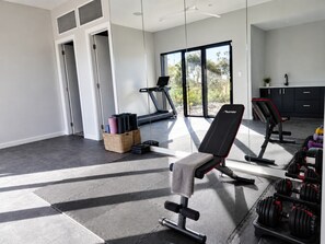A modern gym with exercise equipment, a treadmill, and a large window. - Escape To The Bay – Grand Luxury with heated pool and spa (Nelson Bay)