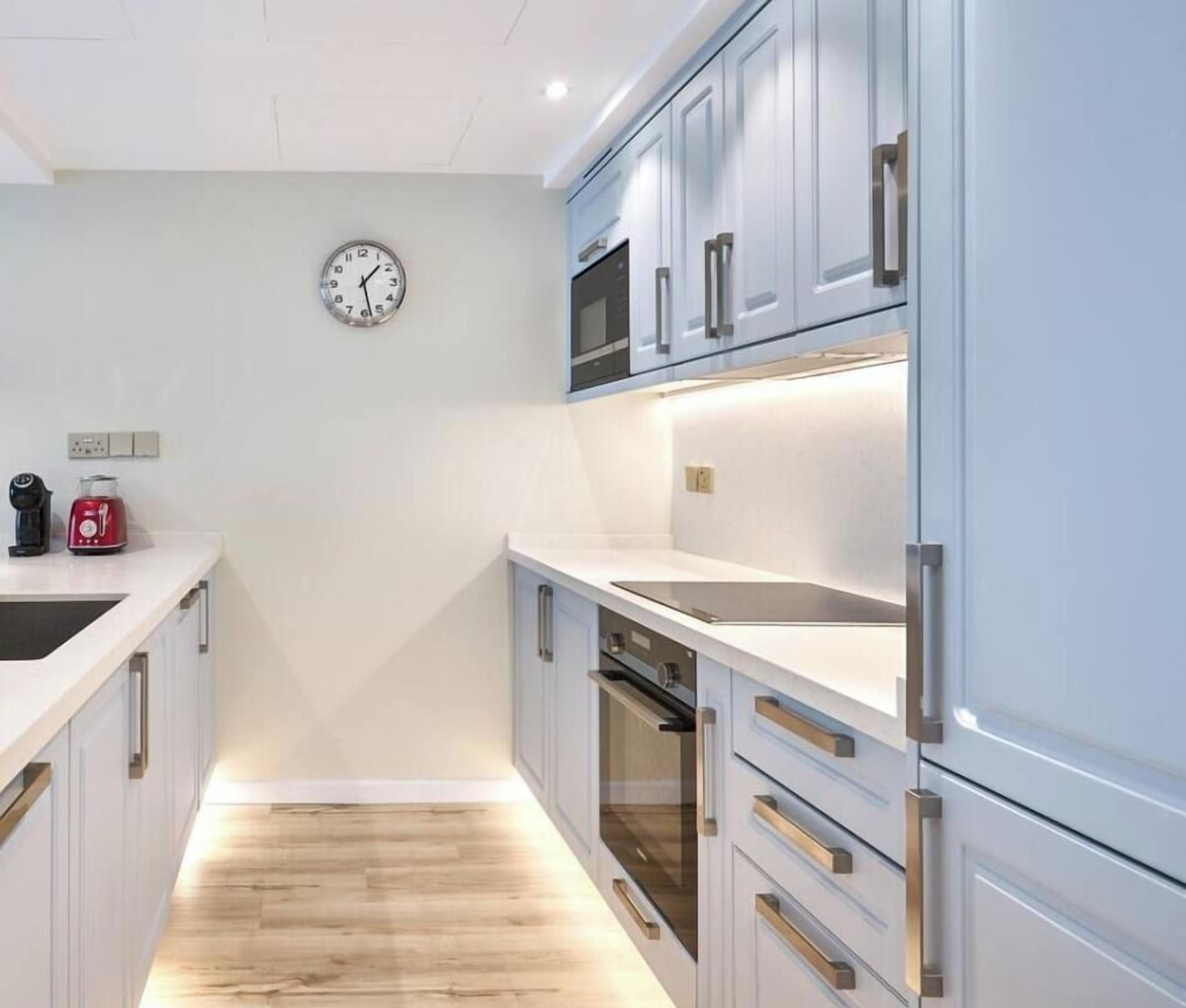 A modern kitchen with white cabinetry, stainless steel appliances, and a wooden floor.
