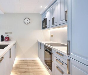 A modern kitchen with white cabinetry, stainless steel appliances, and a wooden floor. - Elegant 1BR Apartment | Prime Greens Community (Dubai)