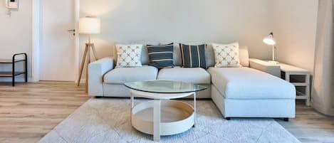 A modern living room with a sofa, a glass coffee table, a lamp, and a small side table.