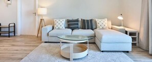 A modern living room with a sofa, a glass coffee table, a lamp, and a small side table. - Elegant 1BR Apartment | Prime Greens Community (Dubai)