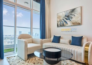 A modern living room with a sofa set, a glass coffee table, and a city view through large windows. - Stylish 1BR w/ Huge Balcony | Desert City Stays (Dubai)