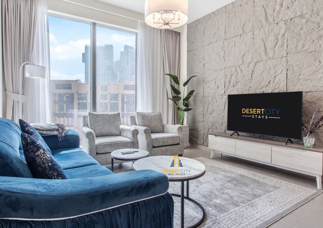 Un salon moderne avec un canapé bleu, des fauteuils gris, une table basse et un téléviseur à écran plat.