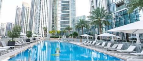 A swimming pool with lounge chairs and umbrellas, surrounded by high-rise buildings.
