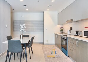 A modern kitchen with a dining area, featuring a built-in oven, microwave, and a dining table with chairs. - Plenty of Restaurants | All Bills Included (Dubai)