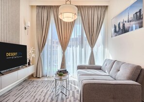 Una habitació d'hotel moderna amb un gran televisor de pantalla plana, un sofà, una taula auxiliar petita amb llibres i un quadre de paisatge urbà a la paret.