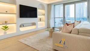 Ein modernes Wohnzimmer mit Flachbildfernseher an der Wand, einer Couch mit dekorativen Kissen, einem runden Couchtisch und einem großen Fenster mit Blick auf die Stadt.