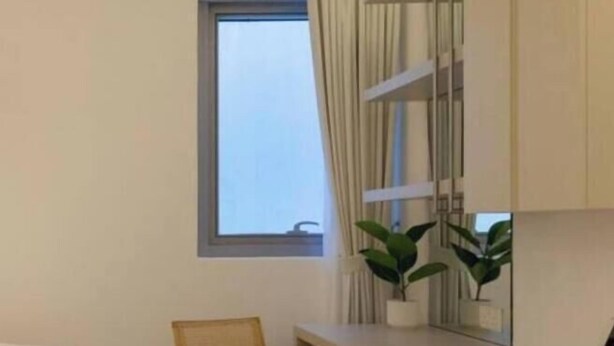 Ein Schlafzimmer mit einem Bett, einem Schreibtisch mit Schubladen, einem Stuhl, einem Fenster mit Vorhängen und einer kleinen Pflanze auf dem Schreibtisch.