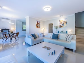 A modern living room with a white sofa, a coffee table, and a dining area with chairs and a table. - Boavista - Golf View Villa (Lagos)