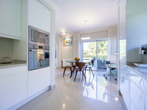 A modern kitchen with built-in appliances, a dining area with a table and chairs, and a sliding glass door leading to an outdoor space. - Boavista - Golf View Villa (Lagos)