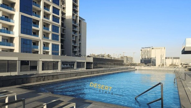 Piscina com superfície de água azul cristalina, rodeada por um edifício moderno com varandas.