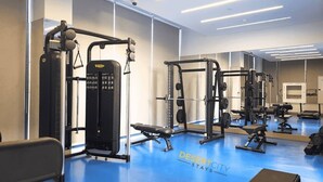 Uma academia com diversos equipamentos de exercício, incluindo máquinas de musculação e pesos livres, sobre um piso azul.