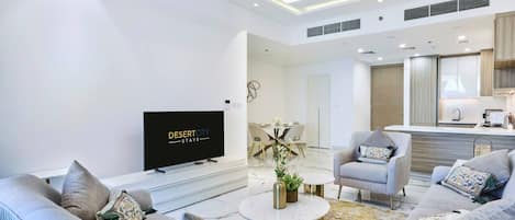 Una sala de estar moderna con un televisor de pantalla plana, dos sofás, una mesa de centro y un comedor con candelabro.