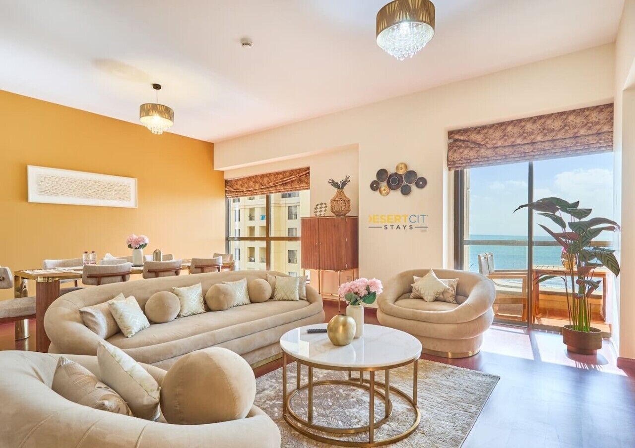 Een ruime woonkamer met een grote bank, een ronde salontafel en uitzicht op de oceaan door grote ramen.