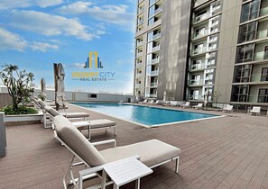 A rooftop pool area with lounge chairs and a view of a high-rise building. - 1 BR Near Downtown | Free Parking | Nice View (Dubai)