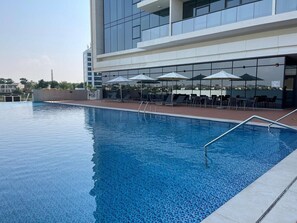A swimming pool with a modern building in the background. - Luxurious Waterfront 2-Bedroom Apartment in RAK (Al Riffa)