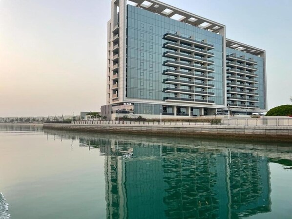 Un immeuble moderne de grande hauteur, doté d’une façade en verre, situé à proximité d’une étendue d’eau calme.