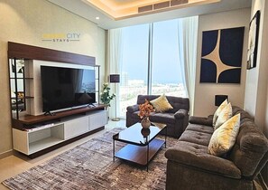 Una sala moderna con televisor de pantalla plana, un sofá, una mesa de centro y un ventanal con vista a la ciudad.