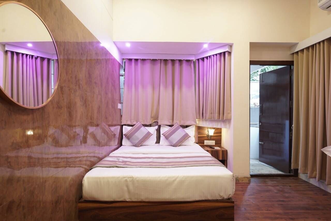 A bedroom with a bed, a bedside table, a mirror, and curtains.