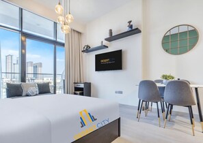Quarto de hotel com cama, escrivaninha, cadeiras, televisão e vista para a cidade.