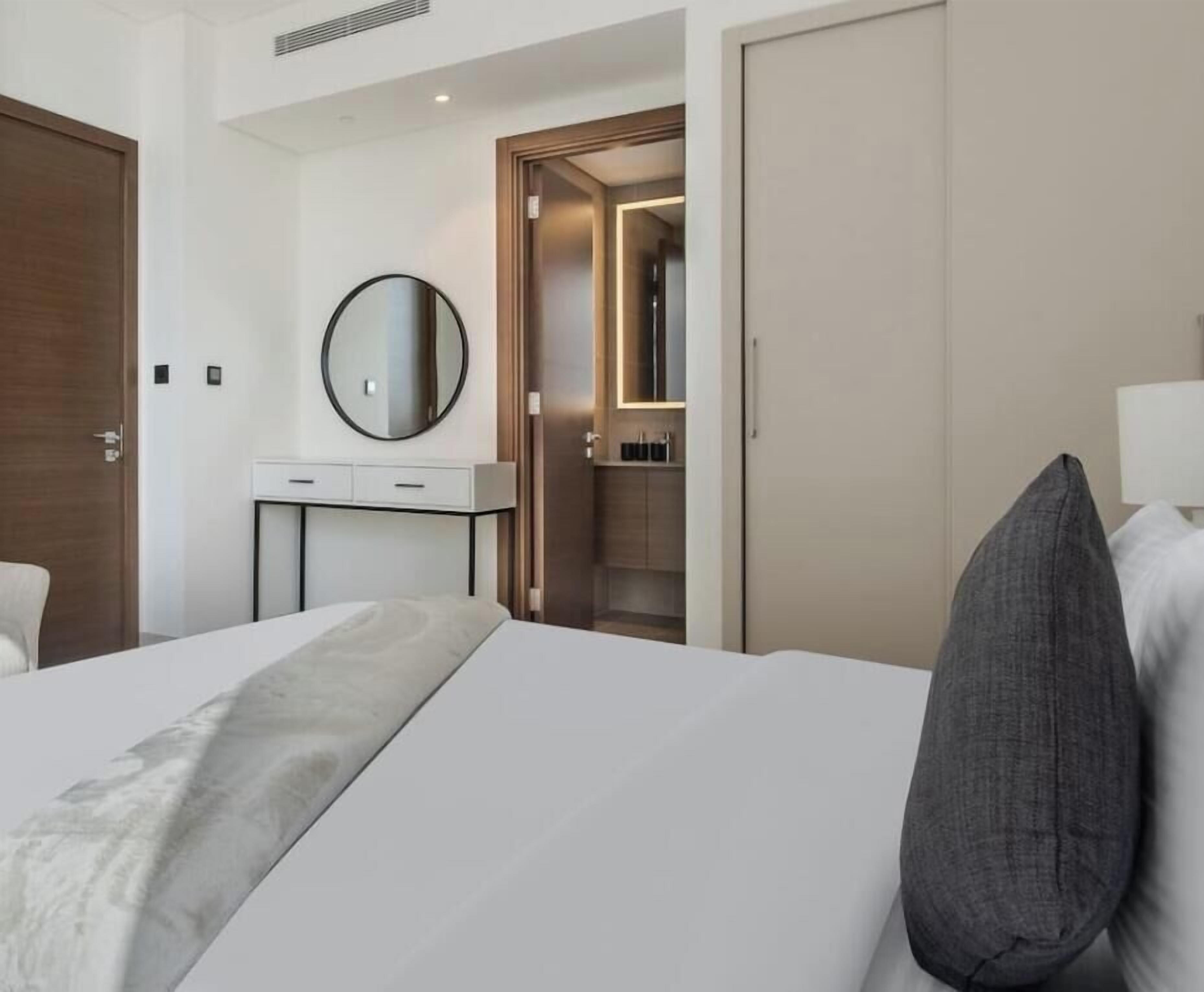A hotel room with a bed, a bedside table, a mirror, a wardrobe, and a bathroom visible through an open door.