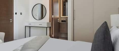A hotel room with a bed, a bedside table, a mirror, a wardrobe, and a bathroom visible through an open door.