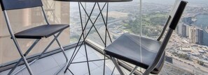 Ein hoher Balkon mit zwei Stühlen und einem Tisch, mit Blick auf eine Stadtlandschaft.