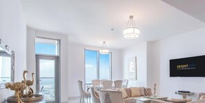 Ein modernes Wohnzimmer mit Essbereich, großen Fenstern und einem montierten Fernseher, der 'DESERTCITY STAYS' anzeigt.
