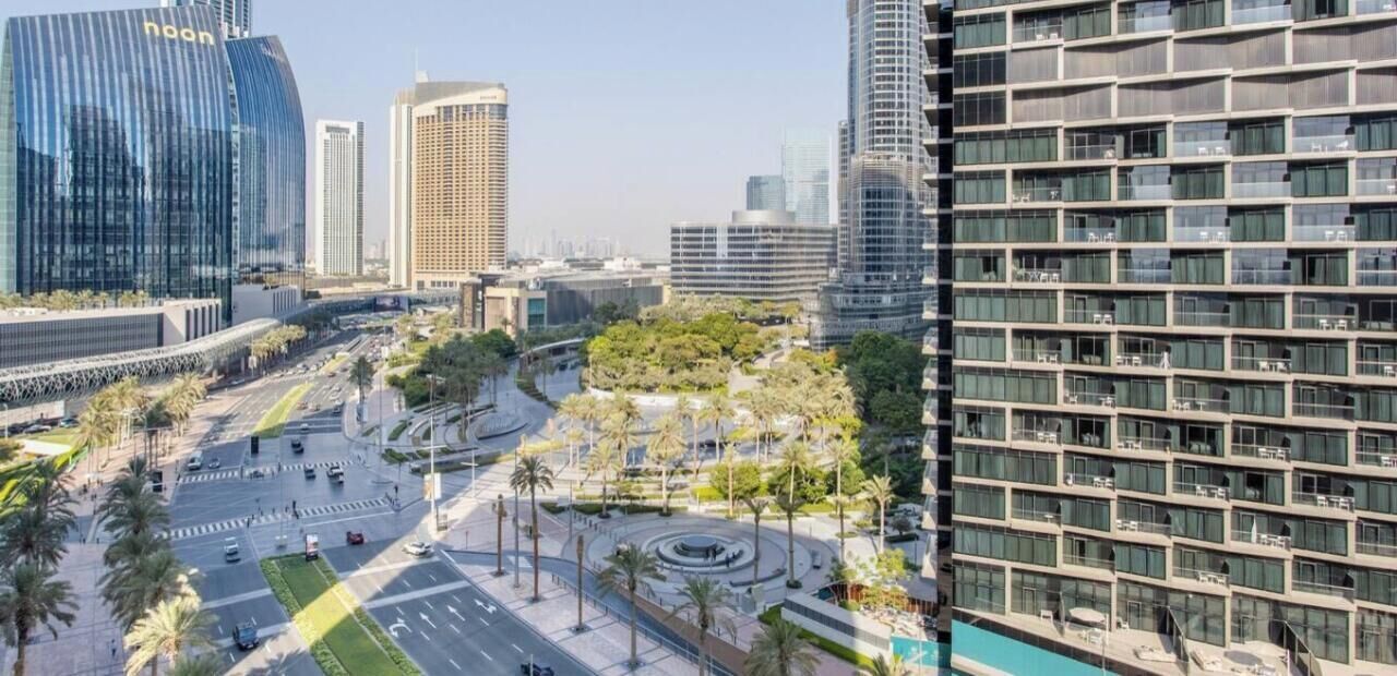 Zona urbana moderna con edificios altos, una glorieta central y un hotel con fachada de diseño geométrico.