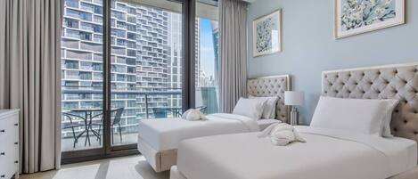 A hotel room with a large bed, a smaller bed, a desk, and a balcony with a city view.